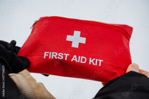 An individual is holding a bright red first aid kit that prominently features a white cross emblem on its surface, indicating its purpose for emergency medical situations photo