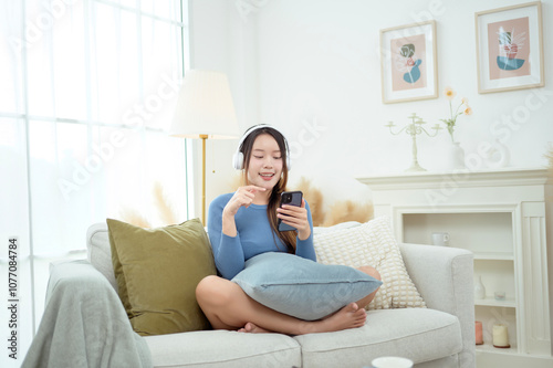 Free Download Young Asian woman wearing headphones enjoying music in living room at home - GFXLoad