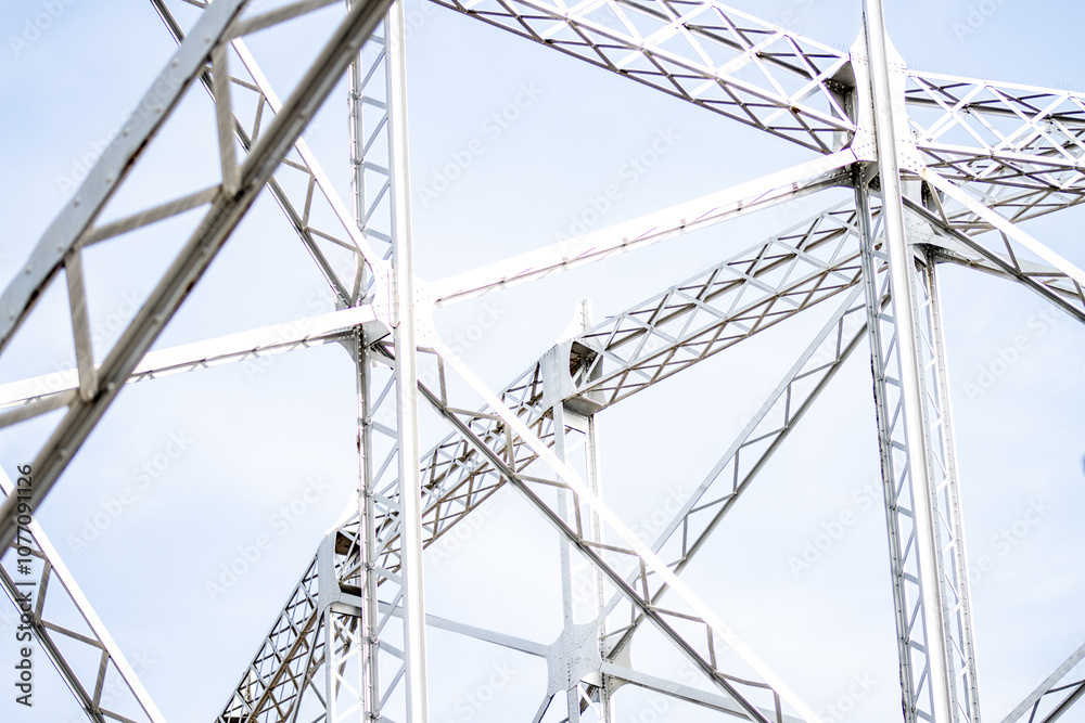 Detailed view of a metal truss structure with beams and crisscross patterns. Close-up of metal truss framework with intersecting beams against a light sky Detailed view of a metal truss structure with beams and crisscross patterns. Close-up of metal truss framework with intersecting beams against a light sky