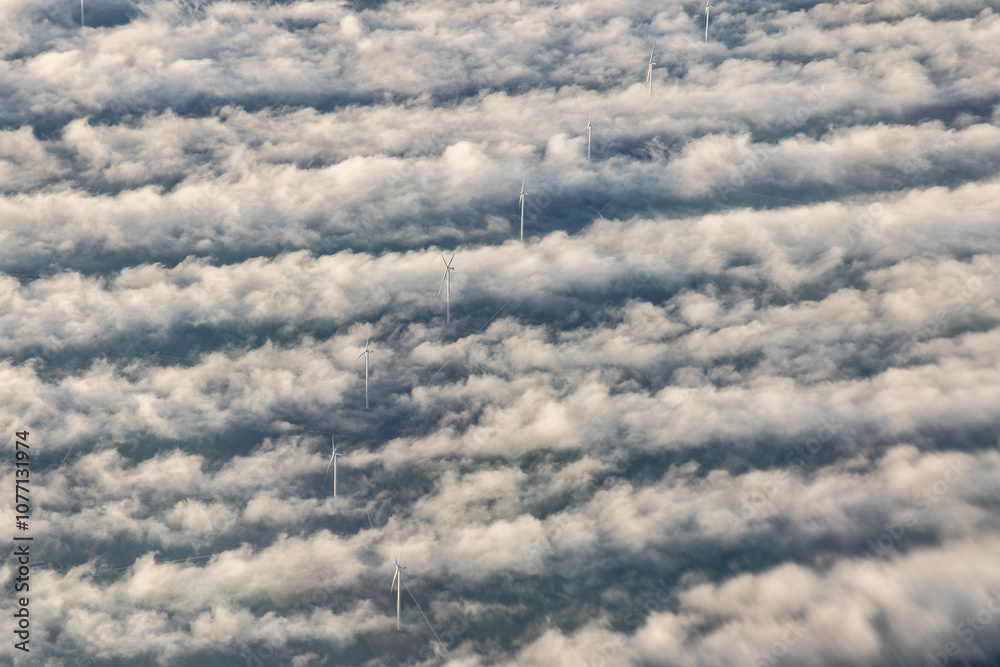 Fototapeta premium Windmills, windturbines above the fog clouds creating vortex trails