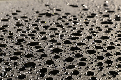 Regentropfen auf einem schwarzen Glas wirken durch seitliche Beleuchtung wie schwarze Wassertropfen unterschiedlicher Größen photo