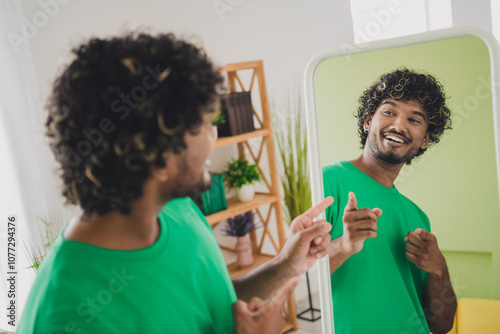 Photo of nice young man point fingers self mirror wear t-shirt weekend green interior apartment indoors photo