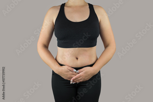 Close up of woman in sportswear posing on grey isolated background and touching lower abdomen because of pain. Front crop. Female pain. Pain lower abdomen.