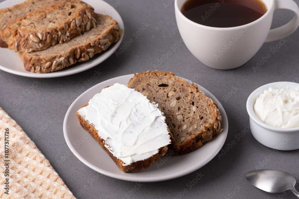 Slices of whole grain bread topped with cream cheese on a plate in a cozy kitchen setting Slices of whole grain bread topped with cream cheese on a plate in a cozy kitchen setting