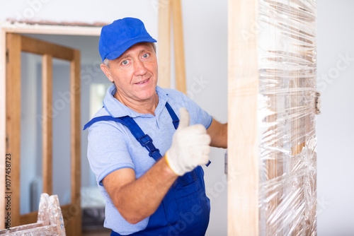 Wallpaper Mural Happy male carpenter in uniform holding a wooden door for installing indoors Torontodigital.ca