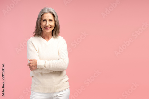 Smiling, senior, gray haired woman wearing white sweater, with crossed arms looking at camera