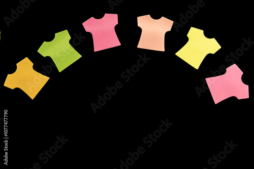 Six blank sticky note pads in the shape of T-shirts, arranged in an arc with colors in salmon, orange, yellow, green, and pink. Isolated on a black background for a clean, high-contrast presentation. photo