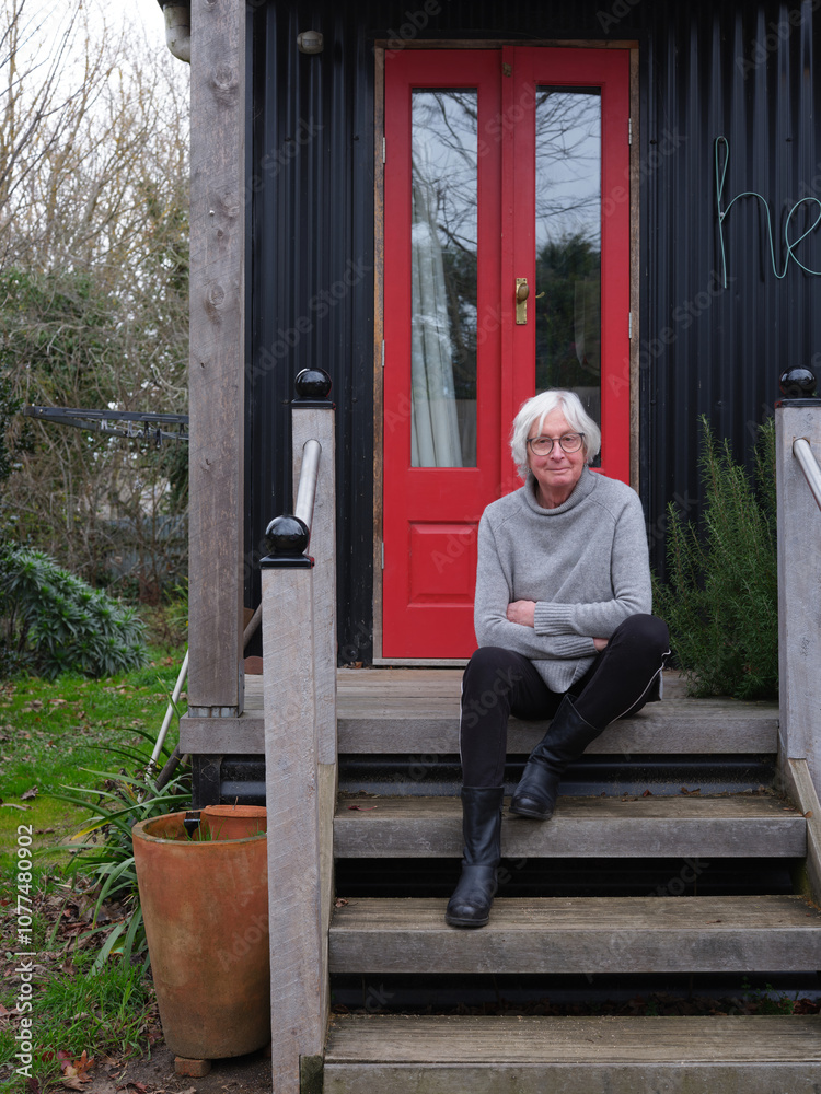 Transgender woman sitting on steps by red door of a charming cottage