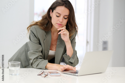 Looking at her mobile phone while scrolling on her laptop