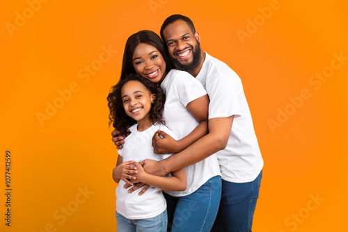 Family Love Concept. Portrait of African American man and woman hugging smiling curly girl standing isolated on yellow studio background. Positive mum and dad posing with daughter at camera