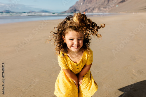 Portrait of cheerful little girl in a yellow dress posing at the beach photo