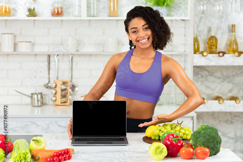 Ordering Food Online. Smiling fit black girl pointing at laptop with blank screen, staying cooking at home, mock up photo