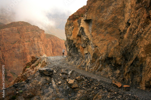 A man walking on An extremely rugged and rocky track among black and red rock mountains photo