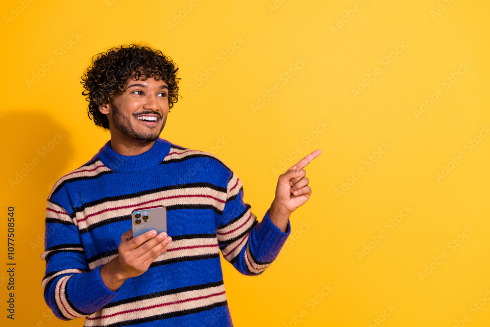 Photo portrait of attractive young man hold gadget point look empty space dressed blue striped clothes isolated on yellow color background Photo portrait of attractive young man hold gadget point look empty space dressed blue striped clothes isolated on yellow color background