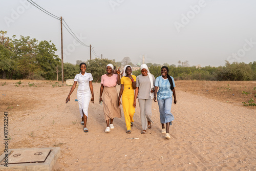 Group of senegalese women walking on a dirt road in senegal, africa photo