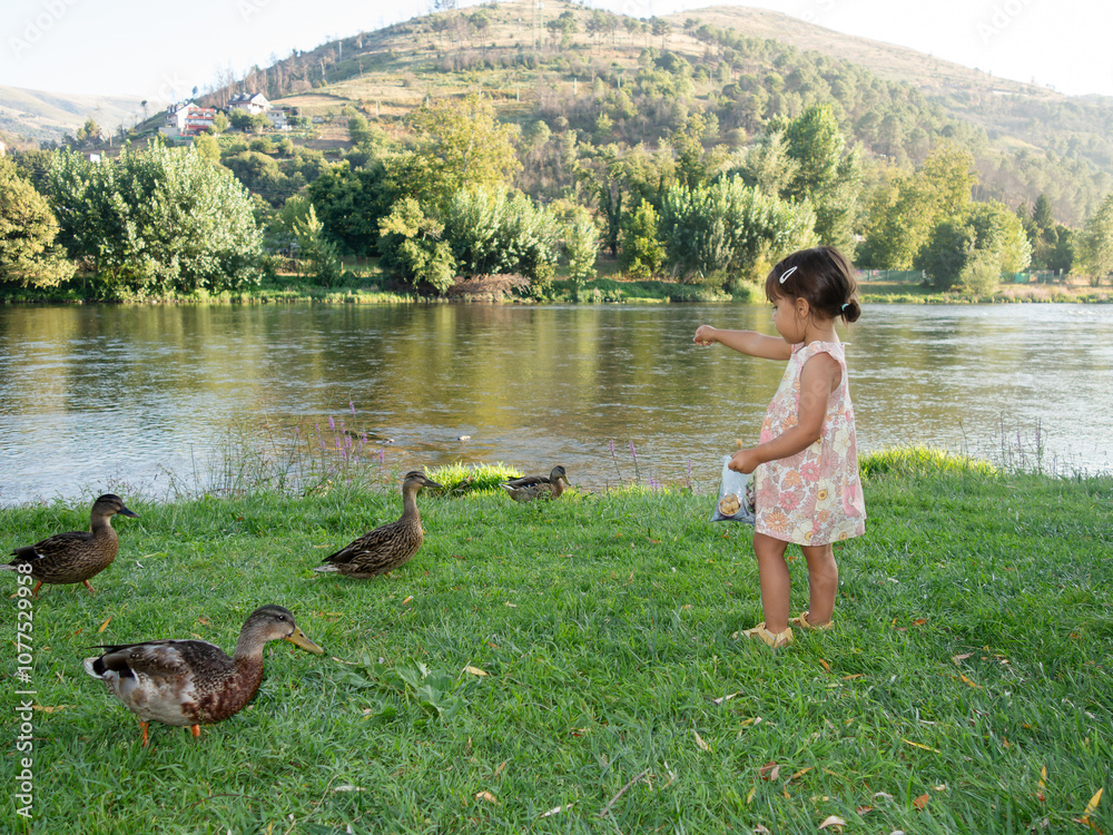 © mahalo studio/Stocksy - Little girl feeding ducks by the river in summer