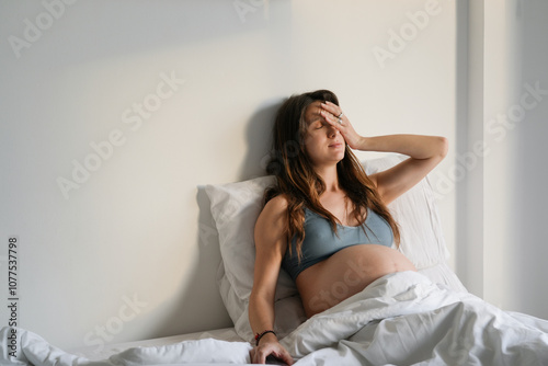 Pregnant woman resting in bed, experiencing fatigue in morning light photo