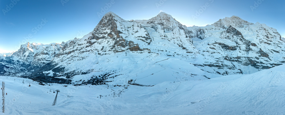Panoramic view of famous snowcovered mountains Eiger, Mönch and Jungfrau (from left to right) in Switzerland with Grindelwald and Wetterhorn (far left) in winter early in the morning against blue sky
