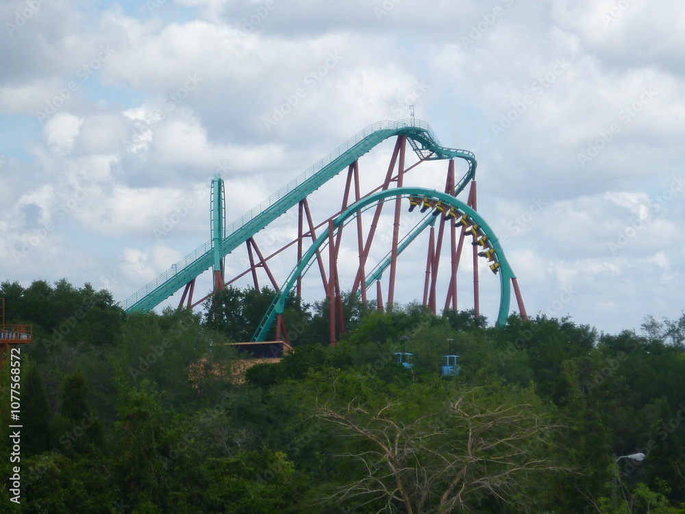 Blue green red rollercoaster with greenery and vegetation, cloudy sky