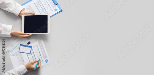 Hands of doctors with tablet and medical insurance form on grey background wi...