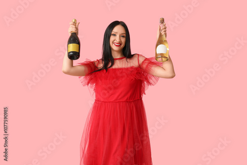 Beautiful young woman with bottles of champagne on pink background