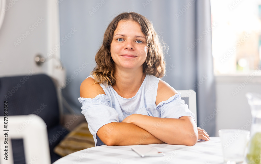 Portrait of young woman sitting near dining table in living room, posing on camera Portrait of young woman sitting near dining table in living room, posing on camera