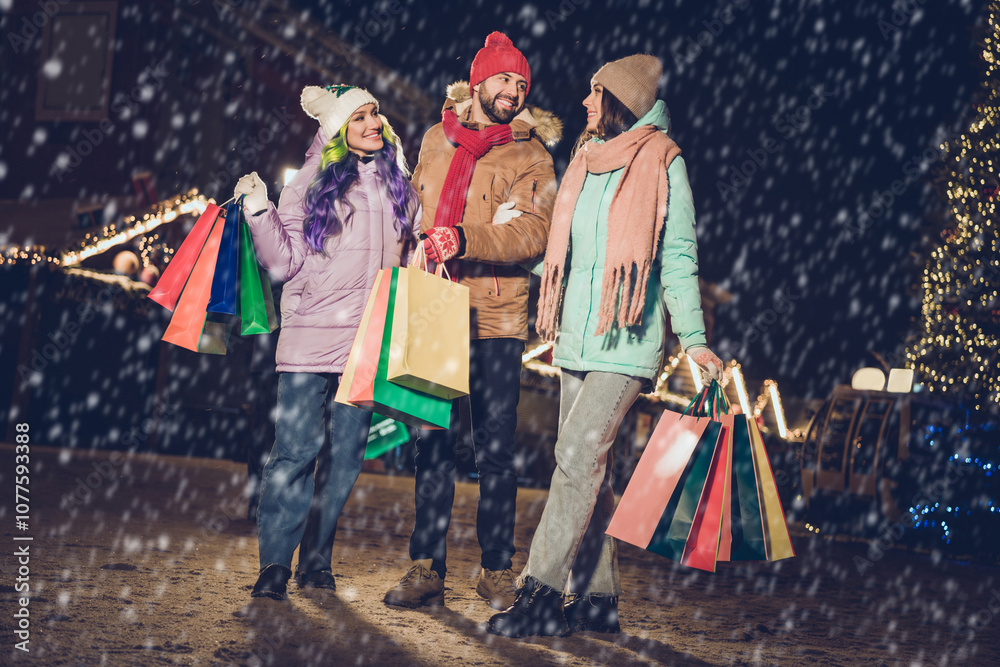 Full size portrait of three positive carefree people hold packages chatting enjoy free time evening outside
