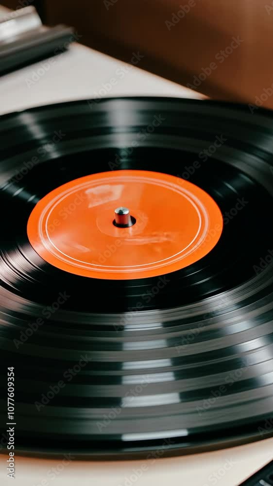 A black vinyl record spins on a turntable, its orange label visible in the center A black vinyl record spins on a turntable, its orange label visible in the center