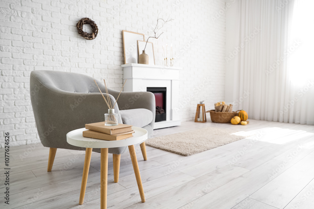 Naklejka premium Interior of stylish room with modern fireplace, armchair and autumn decorations near white brick wall