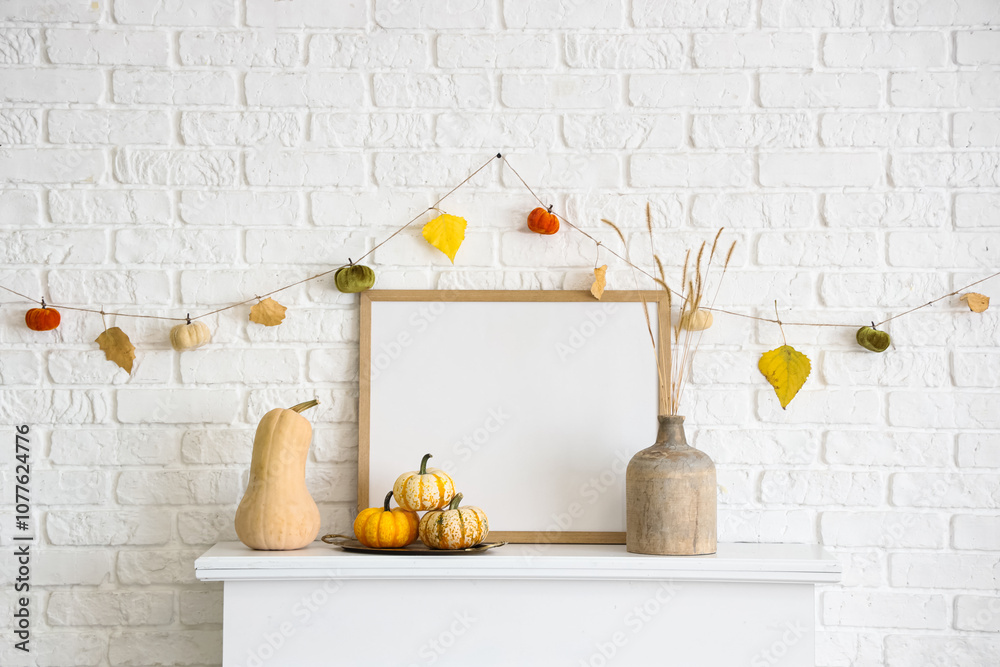 Naklejka premium Frame with pumpkins, vase and autumn garland on modern fireplace near white brick wall