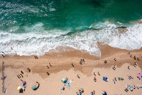 Overhead drone shot of anonymous tourist and colorful parasols on sandy seashore. From above of people enjoying summer vacations at beach during sunny day