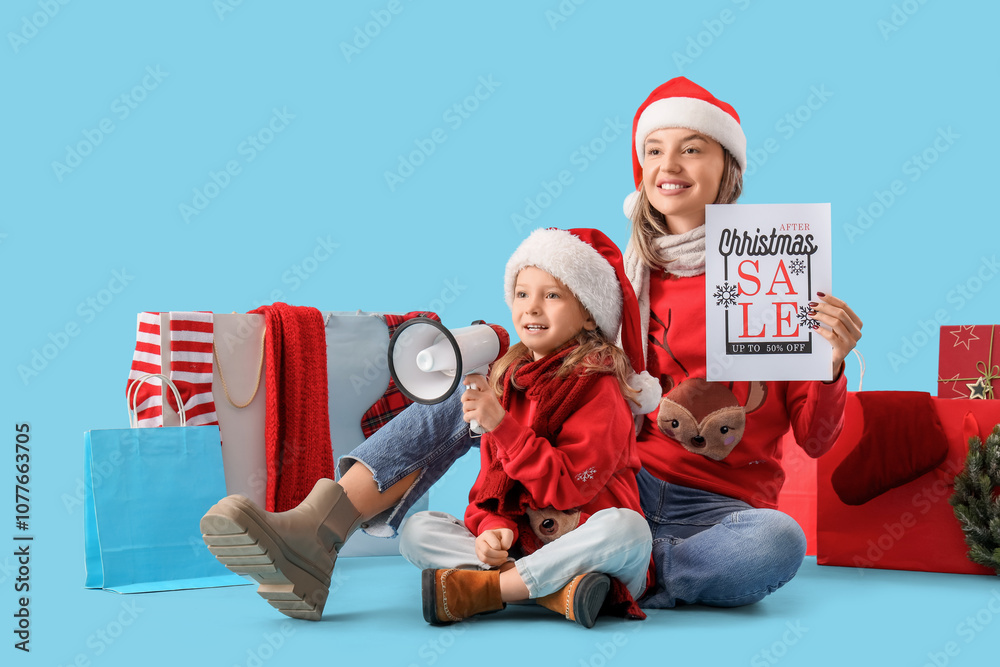 Obraz premium Beautiful young woman holding paper with text CHRISTMAS SALE and her cute little daughter with megaphone on blue background