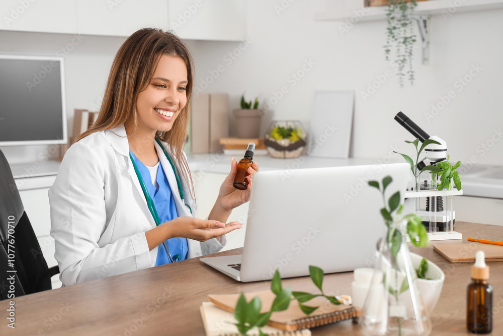 Female homeopathic doctor with dropper bottle video chatting at table in office Female homeopathic doctor with dropper bottle video chatting at table in office