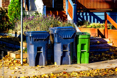 Green garbage systems: compost (green) and recycling (blue) bins out for curbside pick up in the  Toronto Beaches on a fall morning with autumn leaves room for text photo