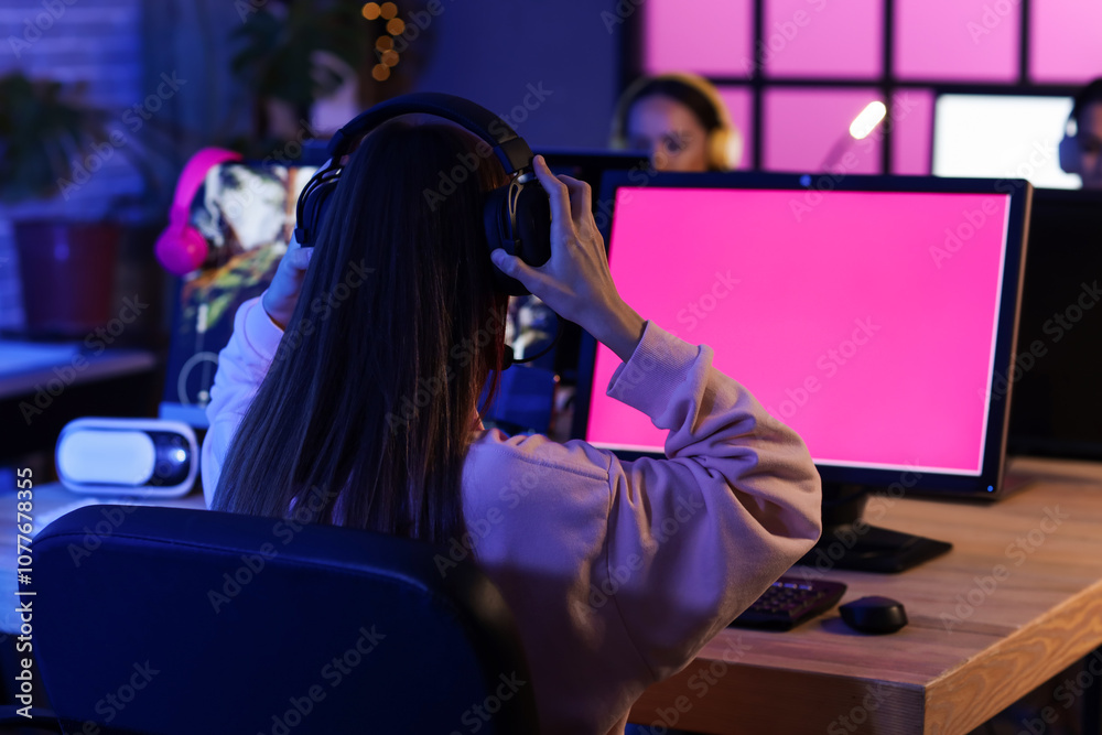 Young woman with headphones playing computer game in club at night, back view Young woman with headphones playing computer game in club at night, back view