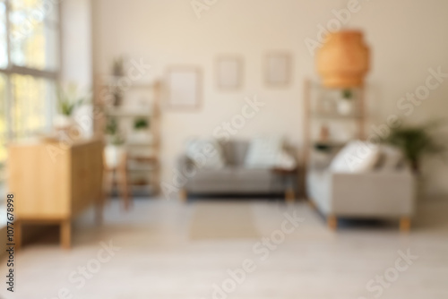 Blurred view of light living room with grey sofas, shelf units and plants