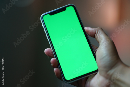 Hand holding smartphone with green screen display. Focus selected