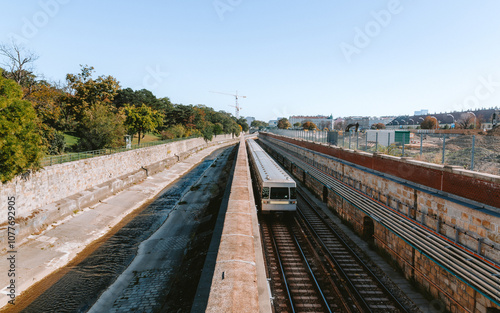 Photography Subway train passing between a small river and a stone wall in vienna on a sunny