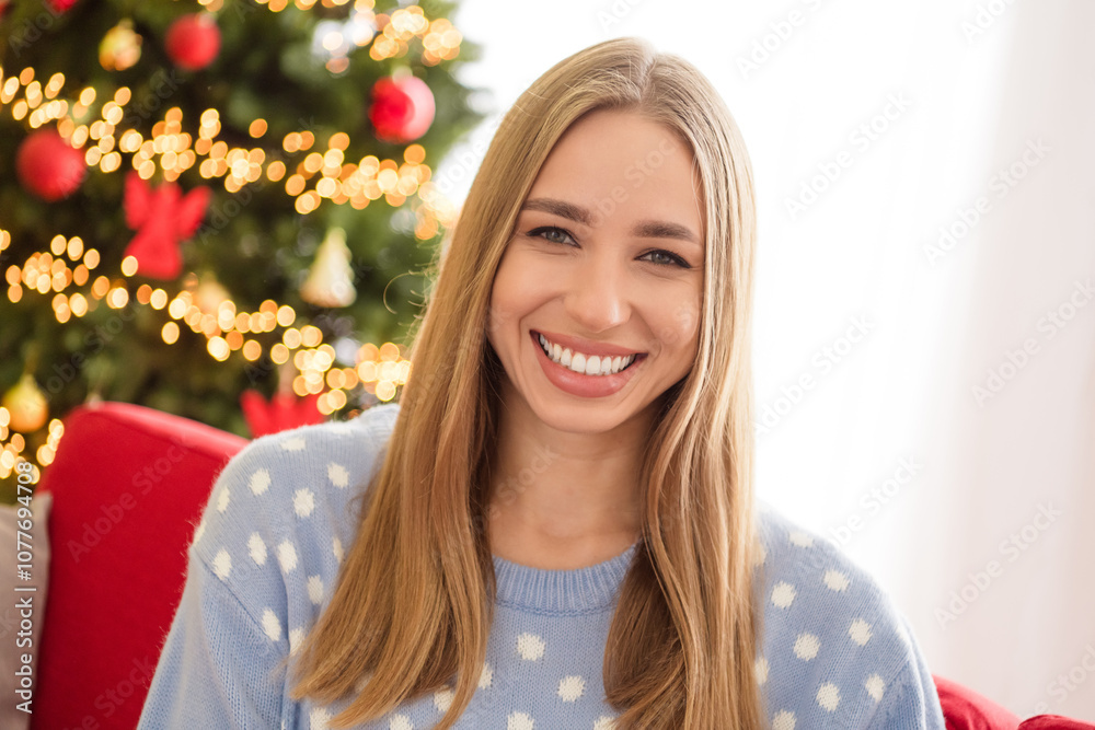Photo portrait of blonde hair happy girl wearing blue warm sweater near fir tree bright lights garland and sitting comfortable couch Photo portrait of blonde hair happy girl wearing blue warm sweater near fir tree bright lights garland and sitting comfortable couch