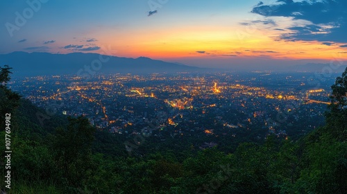 A panoramic view of a city at dusk, with the lights of the cityscape glowing against the fading sunlight and a backdrop of mountains.