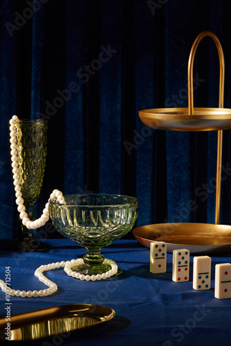 The prussian blue backdrop in a template photo with the party concept, close-up glass cups containing pearl strings, next to brass trays with different shapes, and some dominoes on the blue surface. photo