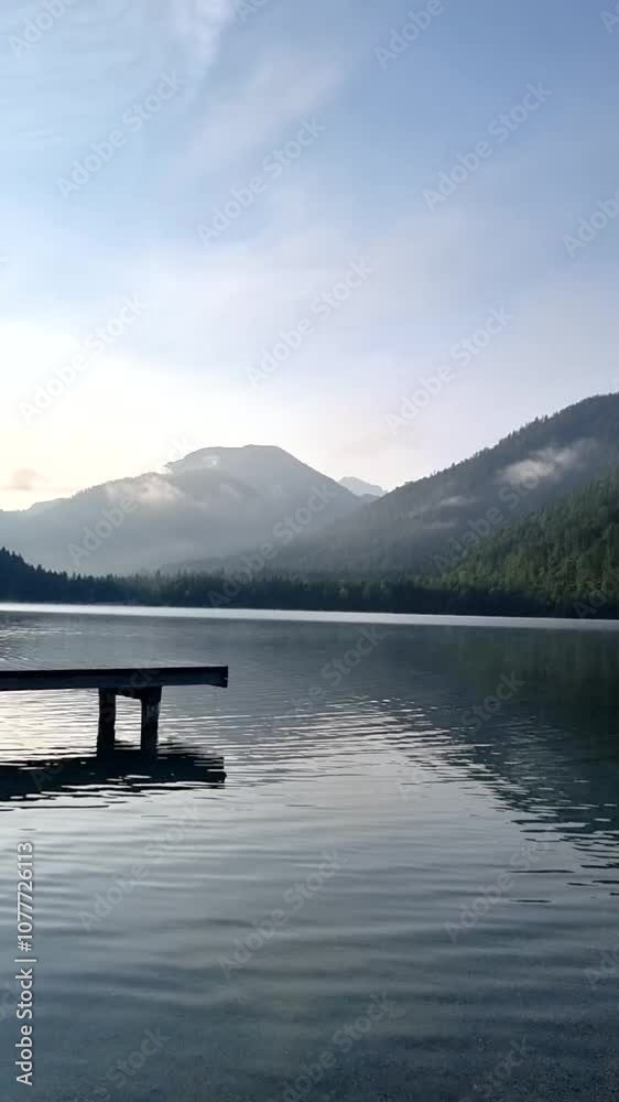 A serene morning unfolds as still waters cradle the reflections of towering mountains. A wooden dock invites peaceful exploration amidst nature's beauty at sunrise. Plansee Austria A serene morning unfolds as still waters cradle the reflections of towering mountains. A wooden dock invites peaceful exploration amidst nature's beauty at sunrise. Plansee Austria