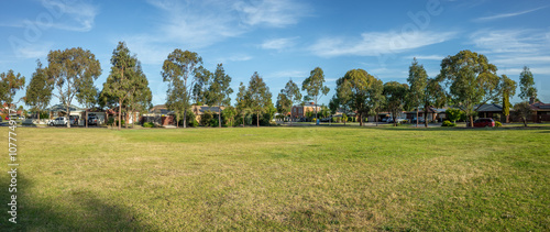 Photography Panoramic of large open space with green grass lawn with some residential houses in the background