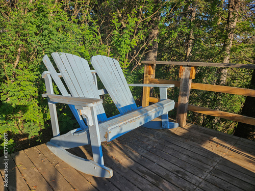 Two empty wooden Adirondack patio chairs painted blue sitting next to each other on a wooden outdoor patio.