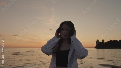 Portrait of beautiful young girl wearing headphones on sea against background of beautiful sunset