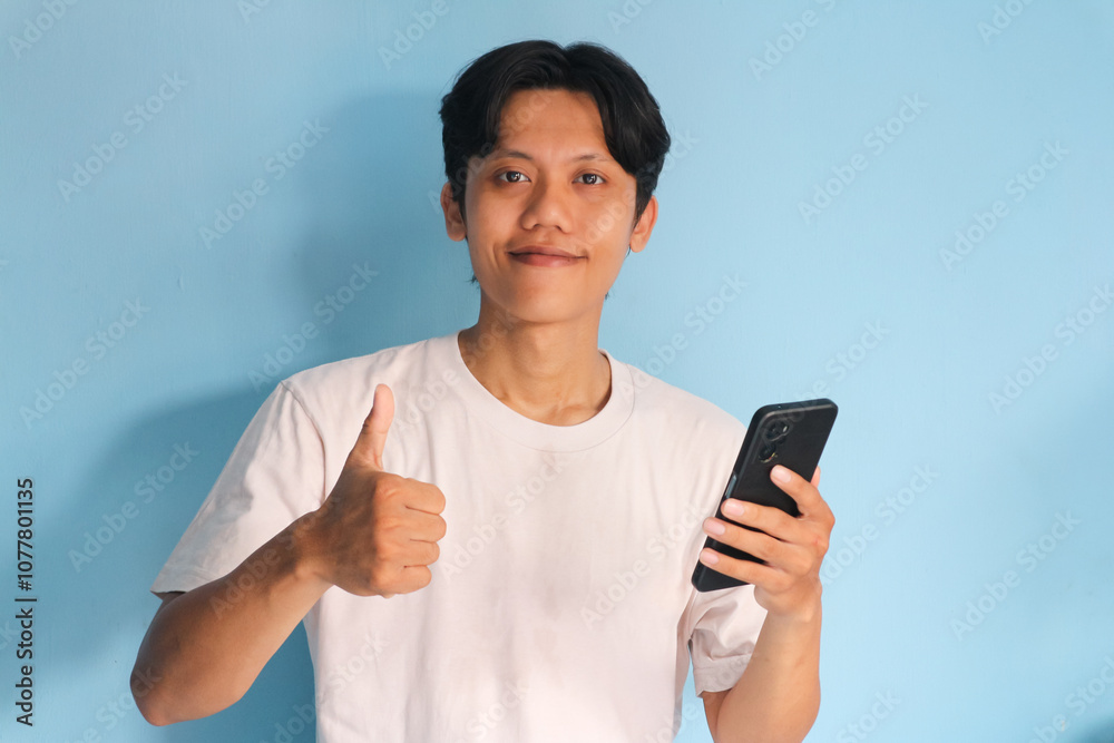 Young Asian man holding his mobile phone with happy expression and thumb up gesture Young Asian man holding his mobile phone with happy expression and thumb up gesture