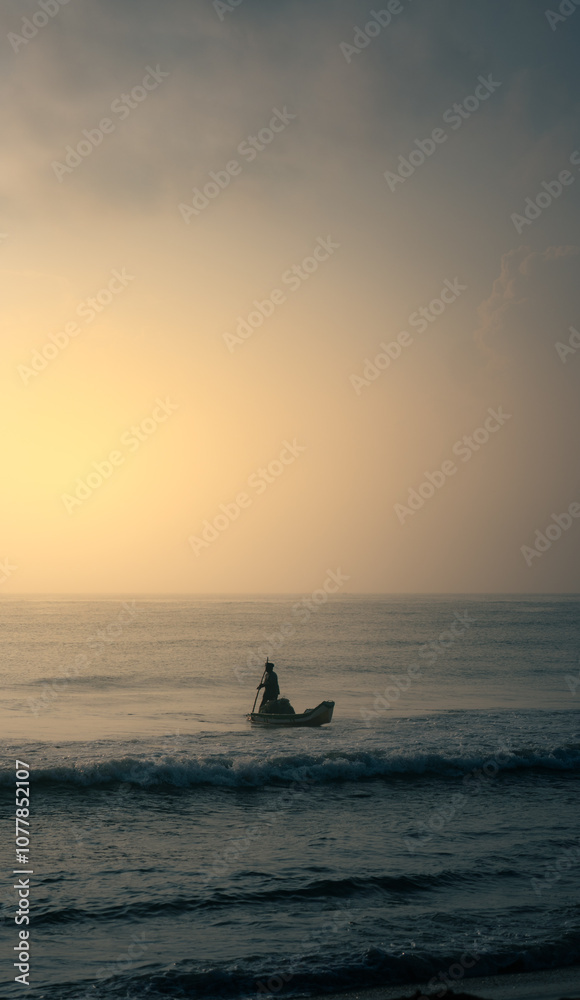 Fototapeta premium A lone fisherman rows his small boat towards the horizon, silhouetted against a stunning sunrise. A timeless scene of human resilience and connection with nature, perfect for travel, documentary, and 
