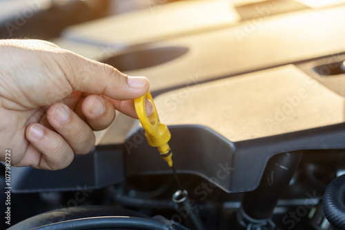 Car owner pulls out the dipstick to check engine oil levels, highlighting the importance of regular oil maintenance for optimal engine performance and vehicle longevity photo