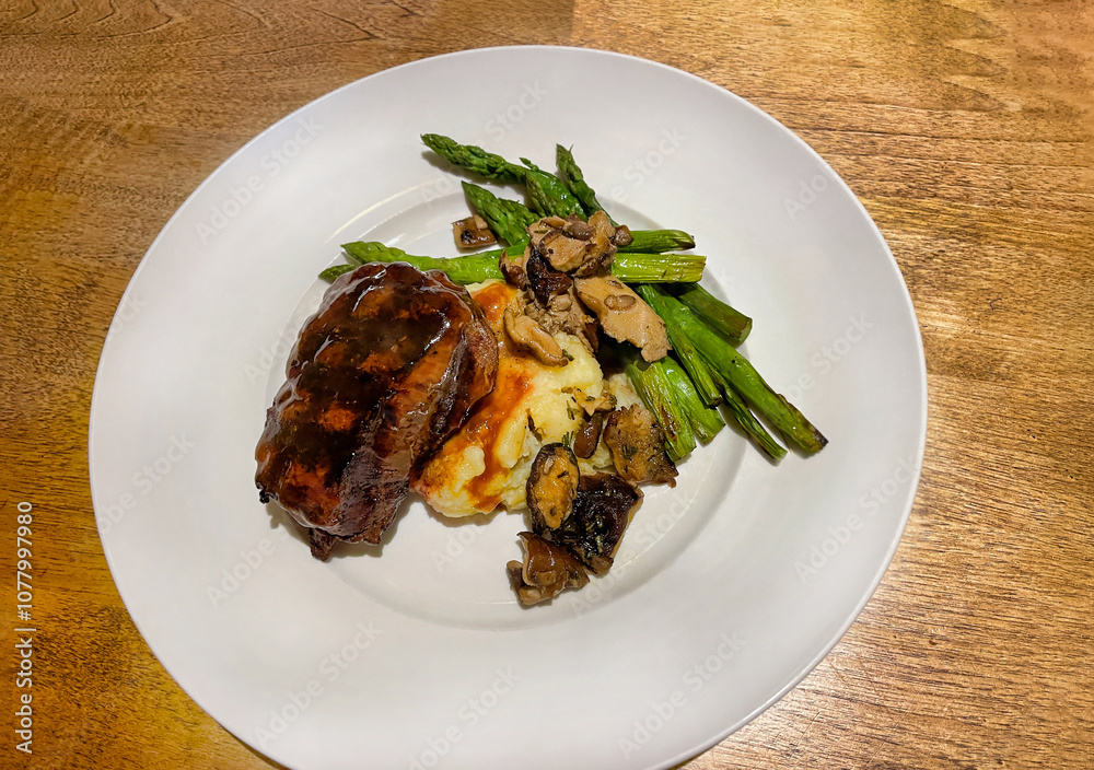 Grilled filet mignon served with mashed potatoes and asparagus and topped with gravy and sautéed mushrooms. Grilled filet mignon served with mashed potatoes and asparagus and topped with gravy and sautéed mushrooms.