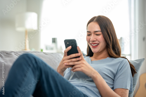 Asian beautiful woman sitting on sofa and using mobile phone in house.